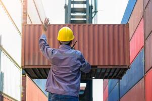 Dock supervisor in yellow hard hat and uniform directing container loading with walkie talkie and hand gesture at shipping container yard. photo