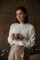 Cozy indoor moment with a woman enjoying coffee while dressed elegantly in a warm sweater and satin skirt during autumn photo