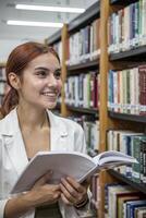 Young woman with red hair smiles while holding a notebook in a vibrant library filled with books during the day photo