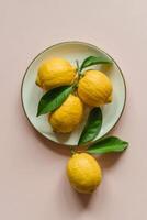 Fresh yellow lemons arranged artfully on a white ceramic plate against a soft pink background create an inviting and minimalist composition photo
