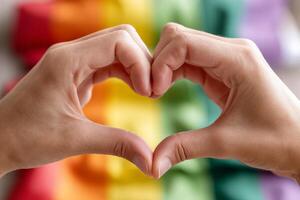 Hands form a heart shape in front of a vibrant rainbow flag celebrating love and diversity photo
