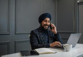 Professional South Asian man engaged in a business conversation while working at a modern white desk photo