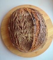 freshly baked artisanal whole wheat sourdough bread with rustic crust cooling on a round metal rack surface side view photo