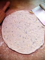rolled khychiny with onion, cheese, and potato filling, resting next to a dough scraper on a prep surface photo