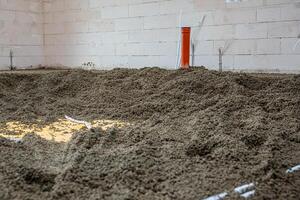 Interior of a construction site featuring an orange vertical pipe, white conduit pipes, loose gravel floor, and light colored concrete block walls. photo