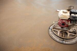 A power trowel with a red engine rests on a damp, even concrete floor, recently smoothed and finished at a construction site. photo