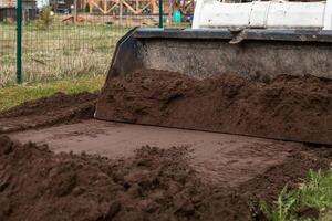 A bulldozer pushes soil across the ground in a fenced area. Blurred structures and construction materials are visible, highlighting earthmoving activity. photo