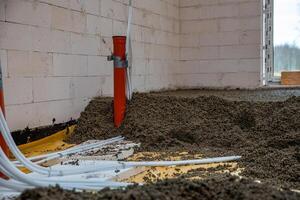 Interior of a construction site with white concrete block walls, an orange pipe taped to the wall, and conduit pipes on a floor of loose aggregate. photo