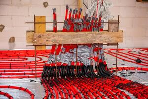 Red and black pipes arranged systematically on a reflective surface, secured with duct tape, with coiled wires and a partially finished wall visible. photo