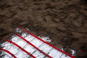 Underfloor heating pipes arranged on reflective insulation, secured by a metal grid, with soil preparation for Estrich concrete visible on the surface. photo