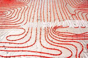 Red underfloor heating pipes arranged in curved patterns over reflective insulation, secured to a grid framework, ready for Estrich concrete application. photo