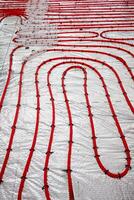 Red underfloor heating pipes arranged in loops, secured with black fasteners on a reflective insulation layer, part of a construction process. photo