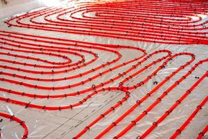 Bright red underfloor heating pipes secured with black clips on a silver reflective surface, prepared for concrete application in a construction project. photo