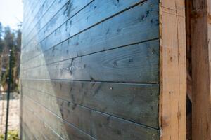 Detailed view of a wooden structure with polished planks, visible grain, knots, and imperfections. Background shows blurred vegetation and sunlight. photo