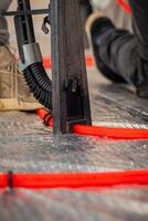 Red underfloor heating pipes are laid on a reflective surface, with a metal tool and a worker's shoe visible, capturing active installation work. photo