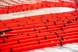 Bright red underfloor heating pipes arranged in a systematic pattern with black clips over a reflective insulating layer, ready for Estrich concrete. photo