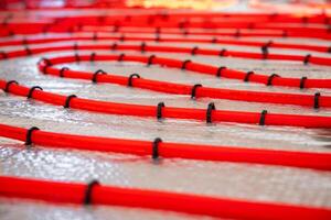 Red underfloor heating pipes arranged in a curved pattern, secured with black clips on a reflective surface, prepared for Estrich concrete application. photo