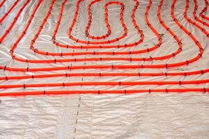 Bright red underfloor heating pipes arranged in loops, secured with black fasteners on a metallic insulation layer, ready for Estrich concrete application. photo