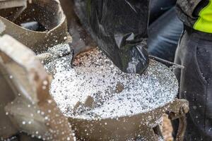 Close up of white granules being poured from a black bag into a metal container, with a worker in high visibility clothing partially visible. photo