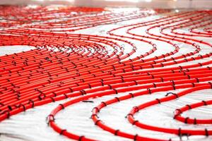 Red underfloor heating pipes arranged in curved patterns, secured with black clips on a light surface, prepared for Estrich concrete application. photo