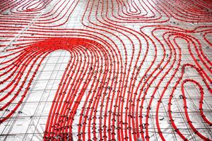 Detailed view of red underfloor heating pipes secured to a metal grid, arranged in a curved pattern on a construction surface for concrete pouring. photo