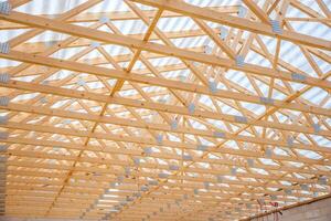 Detailed view of a wooden truss roof structure under construction, with light streaming through translucent panels and concrete walls at the base. photo