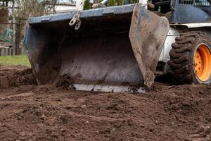 Close up of a white construction vehicle with orange wheels and a metal bucket moving soil. Dirt and mud on the bucket indicate recent use. photo