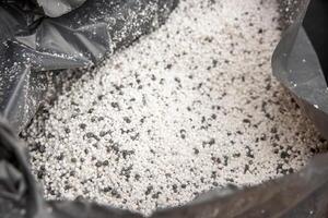 A detailed view of a plastic bag containing small, round, white and black granules. The bag's crinkled edges are visible, emphasizing its durable texture. photo