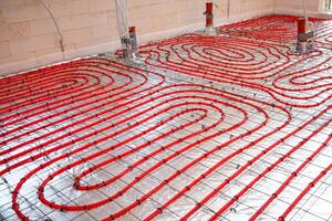 Interior of a construction site showing red underfloor heating pipes arranged in a spiral pattern on a metallic mesh over reflective insulation. photo