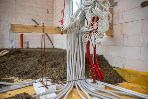 Electrical conduit pipes in white and red emerge from a gravel covered floor, supported by wooden beams and metal rods in an unfinished building. photo