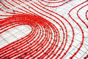 Detailed view of red underfloor heating pipes arranged in a curved pattern, fastened to a metal grid, prepared for a concrete layer application. photo