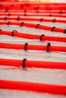 Bright red underfloor heating pipes arranged in parallel lines, secured with black clips on a metallic reflective surface during a heating system installation. photo