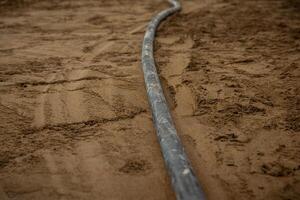 A single underfloor heating pipe curves on compacted sand or soil, with visible ground textures and marks, highlighting early construction stages. photo