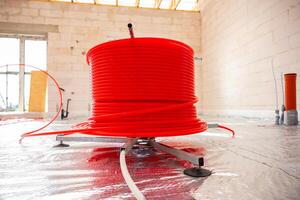 A construction site interior showing red underfloor heating pipes on a metallic surface, light brick walls, and visible ceiling framework in natural light. photo