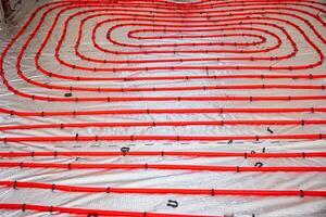Construction site floor with red underfloor heating pipes arranged in loops over a reflective insulation layer, secured with black fasteners. photo
