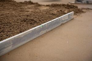 A metal screed tool with a green bubble level levels wet concrete, showing smooth and rough textures during a flooring installation process. photo
