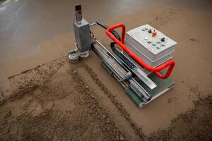 A construction site showing a machine with a red safety handle and control panel, used for leveling screed concrete over underfloor heating pipes. photo