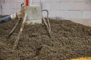 A weathered concrete mixer tool rests in a pile of aggregate material near a partially built brick wall with visible pipes and construction elements. photo