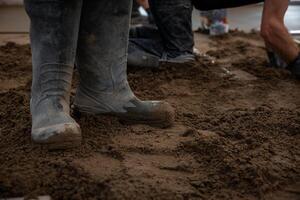 Construction workers install underfloor heating pipes and lay Estrich concrete. Muddy rubber boots stand on damp soil, with tools and materials visible. photo