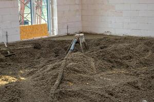 White brick walls and an unfinished floor being leveled with concrete. A hose distributes material, with light entering through a window opening. photo