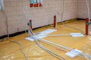 Partially constructed indoor site with white brick walls, yellow floor covering, orange conduit pipes, and white cables secured with foam blocks. photo