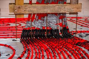 Bright red underfloor heating pipes arranged in a coiled pattern on a reflective surface, secured with duct tape and supported by a wooden frame. photo
