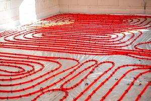 Bright red underfloor heating pipes are arranged in a looping pattern on a reflective surface, secured with clips, in a white block walled construction site. photo