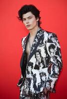 Stylish male model in a graphic-print suit against a red carpet backdrop photo