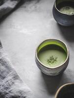 Cup of green tea sits on a table next to two other cups photo