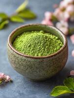 Bowl of green powder is sitting on a table next to some pink flowers photo