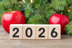 Countdown to the year 2026 with festive decor featuring red apples and evergreen branches nestled on a rustic wooden surface photo