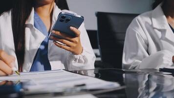 Two doctors are sitting at a table with a laptop and a cell phone video