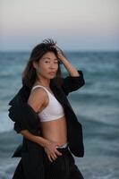 Wind pulls at woman's jacket while waves rise around her, sharp lines softened by water. photo