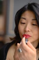 A close-up of an Asian woman applying bold red lipstick. Her eyes are focused on the mirror as she carefully outlines her lips, enhancing her confident and glamorous look. photo